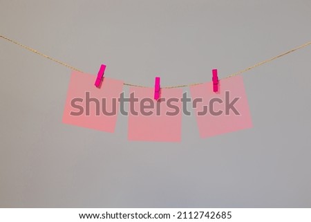 Colored pink paper for notes, notes, office, hanging on colored clothespins on laces, gray background