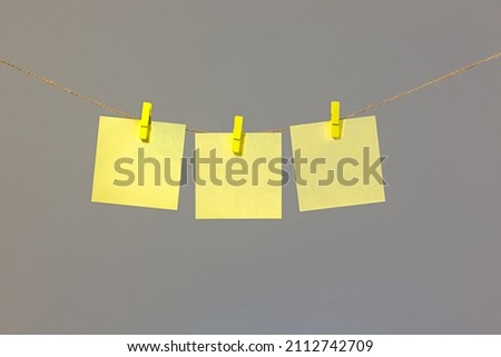 Colored yellow paper for notes, notes, office, hanging on colored clothespins on laces, gray background