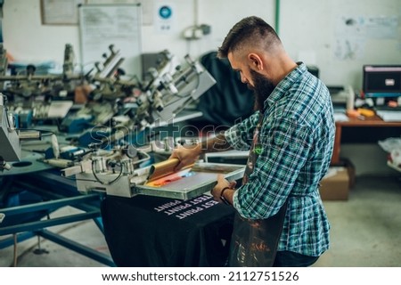 Male worker pressing ink on frame while using the printing machine in a workshop