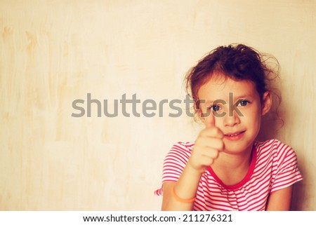 Portrait of a cute kid (girl) showing thumbs up . filtered image