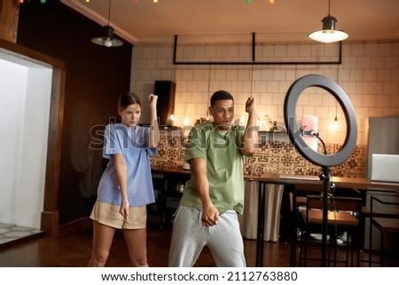 Multiracial blogger couple dancing together during making dance video challenge on smartphone at home. Video blogging. Creative girl and man of zoomer generation creating content for social networks Royalty-Free Stock Photo #2112763880