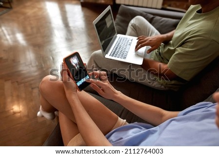 Cropped image of young blogger couple editing video on gadgets for social networks. Video blogging and internet multimedia. Creative girl and guy of zoomer generation creating content on sofa at home