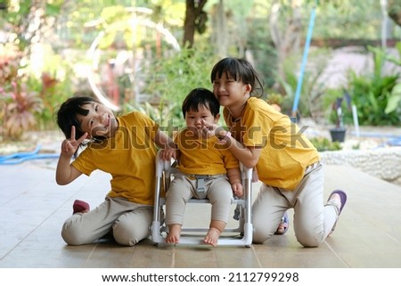 Three siblings of Asian children are smiling as they sit at home.