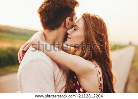 Close-up portrait of a caucasian young loving couple embracing while standing on a roadside. Couple embracing road travel. Sunset scene. Royalty-Free Stock Photo #2112812204
