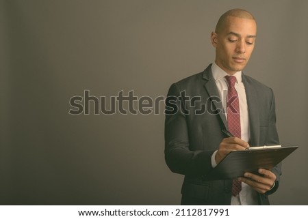 Studio shot of handsome bald businessman wearing suit against gray background