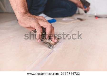 A carpenter filling gaps in wood floors. At the attic, home renovation, restoration or construction. Royalty-Free Stock Photo #2112844733