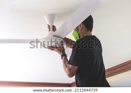 A handyman installs a ceiling fan, tightening the screws of the fan blades. At the living room. Home renovation or construction. Royalty-Free Stock Photo #2112844739