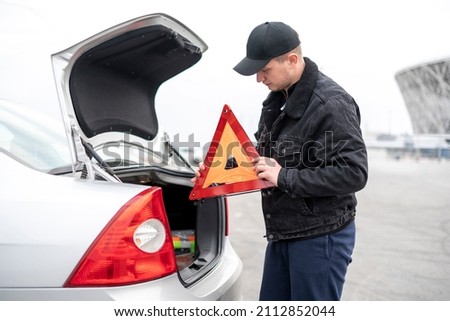 male person hold caution car accident sign and assemble it near the vehicle
