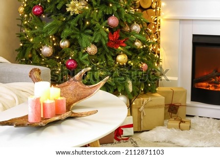 Table with burning candles and deer horn in living room decorated for Christmas