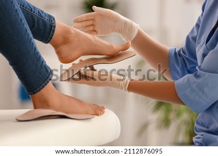Female orthopedist fitting beige insole on patient's foot in clinic, closeup Royalty-Free Stock Photo #2112876095