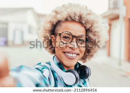 Black cheerful smiling afro latin american woman taking selfie portrait outdoors - Happy smiling girl using her smartphone, eyeglasses and headphones. Technology concept.