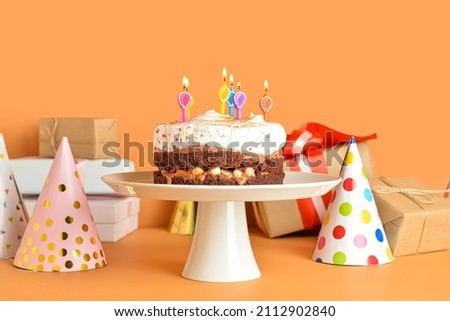 Stand with tasty birthday cake, party hats and gifts on color background