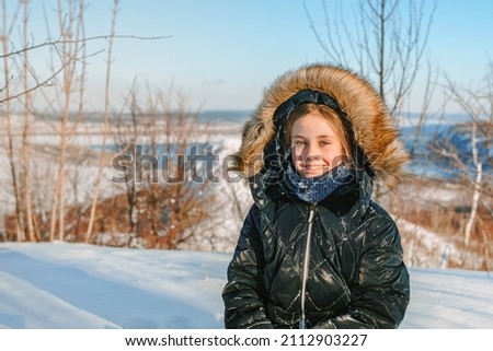 Cute little girl in a warm jacket in a snowy forest on the background of a winter landscape on a high mountain