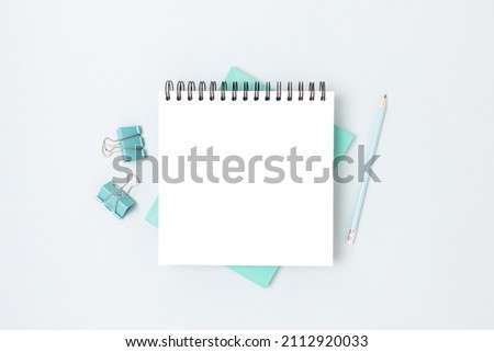 Minimal workspace with square notepad mockup and stationery on a blue background. Monochrome school concept with copyspace. Royalty-Free Stock Photo #2112920033