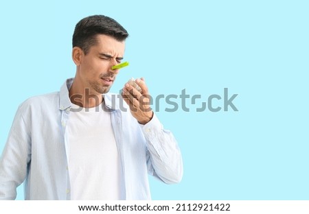 Ill young man with clothespin on his nose against color background