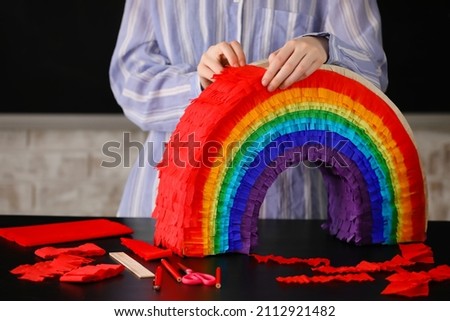 Woman making Mexican pinata in shape of rainbow on table at home