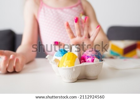 girl paints Easter eggs at home against background of bright decor. kids craft. create art for children Royalty-Free Stock Photo #2112924560
