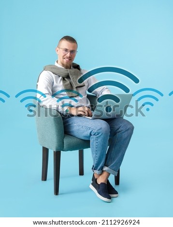 Young man with laptop using wi-fi on color background