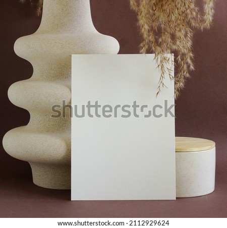 Blank paper mockup template and modern beige vasen with dry grass on brown desk with copy space.
Card Mockup,branding design.
