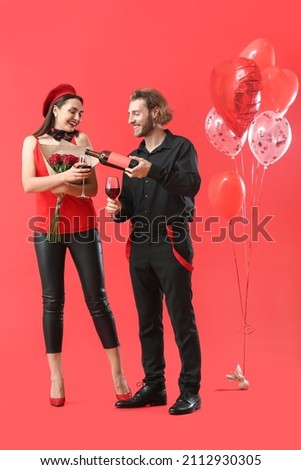 Happy young couple with wine, flowers and balloons on color background. Valentine's Day celebration