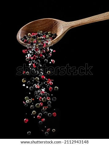 Mix of different peppercorns and salt falling down from the wooden spoon at black background.  Royalty-Free Stock Photo #2112943148