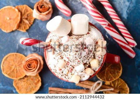 Cup of tasty cacao with marshmallows and candy canes on blue background