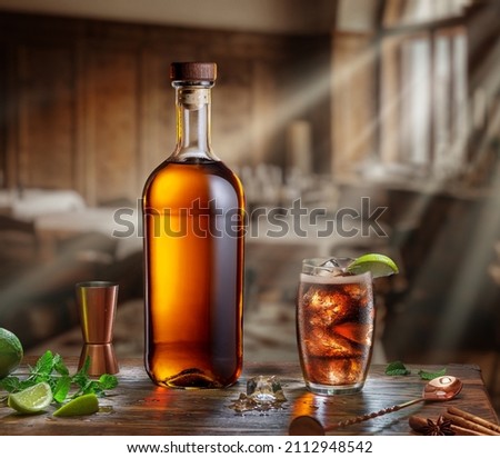 Whiskey bottle and glass of whiskey gleamed in the sun lights from window are on the old wooden table. Blurred interior of pub at the background. Royalty-Free Stock Photo #2112948542