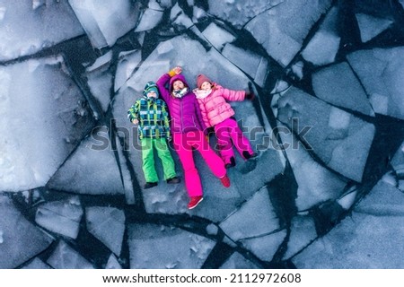 Top view of people lying on ice alone. Woman and children in bright clothes on broken ice block in water. Winter cracked ice on lake with kids. Danger fun. Playing sustainable. Climate global warming. Royalty-Free Stock Photo #2112972608
