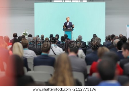 Man giving a speech on a podium in front of an audience in a conference hall  Royalty-Free Stock Photo #2112973196