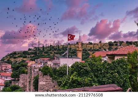 Minaret of mosque and turkish flag crescent moon and stars.Crescent moon is the symbol of islam.photo taken from amasra castle at sunset.birds are flying on the sky background of mosque and flag.