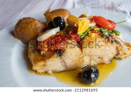 Closeup of a plate of good cod from the Atlantic sea with potatoes, onion, egg, red pepper, olives and coriander