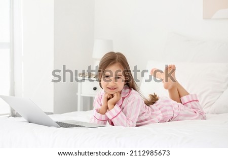 Cute little girl watching cartoons on laptop in bedroom