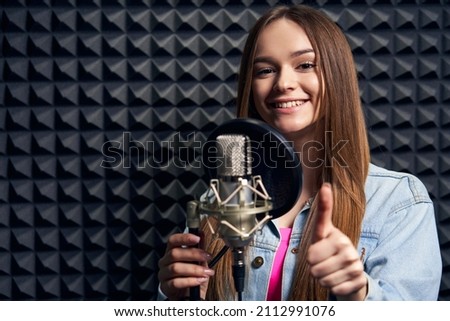 Teen girl in recording studio with mic over acoustic panel background