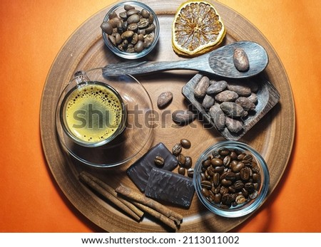 Brown background with bright orange accents and a cup of coffee, chocolate bar, coffee beans, cocoa beans, cinnamon stick.