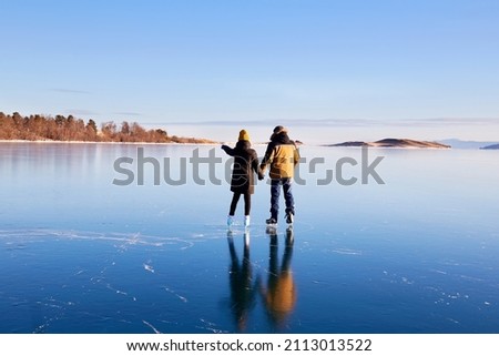 A young couple is skating on the frozen Lake Baikal. Transparent ice. Travel in winter, active recreation, sports.  Royalty-Free Stock Photo #2113013522