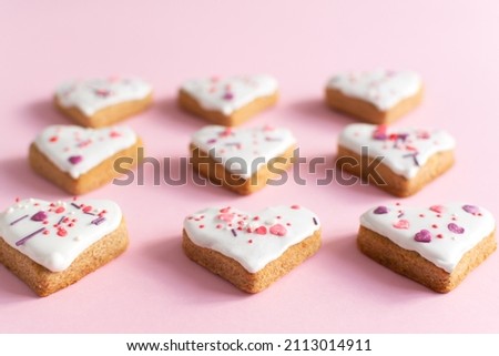 Gingerbread covered with white icing and sprinkling on a pink background. The concept of celebrating Valentine's Day. Horizontal orientation. Selective focus.