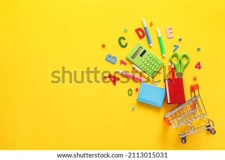 Shopping cart filled with colorful school supplies on yellow background. Copy space. Education, Back to School, Shopping.