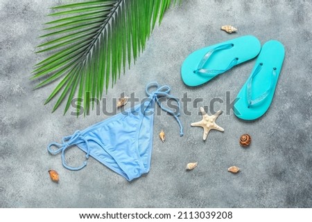 Summer concept with women's beach accessories. Bikini Bikini bottoms, flip flops, decorative palm leaves and seashells on grunge gray background. Top view, flat lay. Textured object, selective focus.