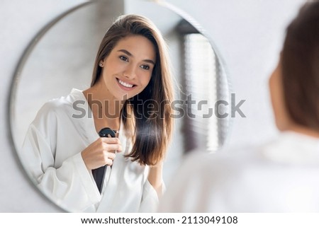 Beautiful Young Woman Applying Moisturising Hair Spray On Ends While Standing Near Mirror In Bathroom, Attractive Lady Enjoying New Hairstyle Cosmetics And Smiling To Her Reflection, Selective Focus Royalty-Free Stock Photo #2113049108