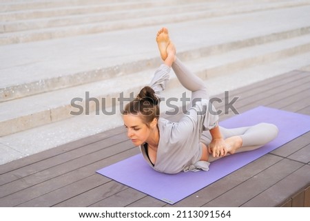 High-angle view of flexible young yogini woman practicing yoga exercisers on fit mat in summer day outdoors in city park. Calm female with beautiful body in sportswear performing asana pose outside