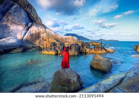 Young woman tourist in red dress standing on Hin Ta Hin Yai with blue sea and sky during summer travel at Koh Samui island, Surat Thani, Thailand Royalty-Free Stock Photo #2113095494