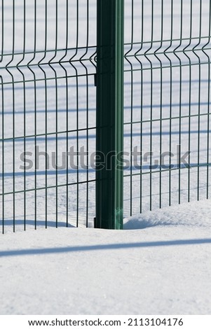 Green metal fence covered with snow, winter.