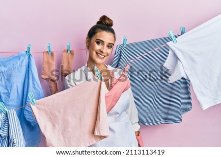 Beautiful brunette young woman washing clothes at clothesline cheerful with a smile of face pointing with hand and finger up to the side with happy and natural expression on face 