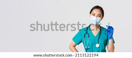 Covid-19, coronavirus disease, healthcare workers concept. Smiling cheerful asian doctor, nurse in medical mask and rubber gloves prepare syringe with vaccine for shot vaccination, white background