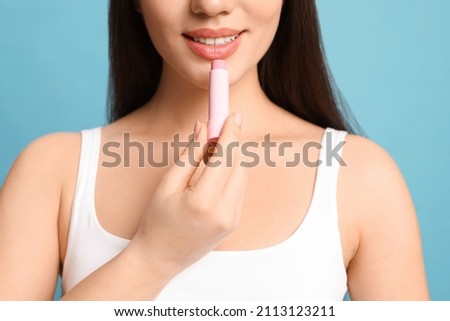 Young woman applying lip balm on turquoise background, closeup