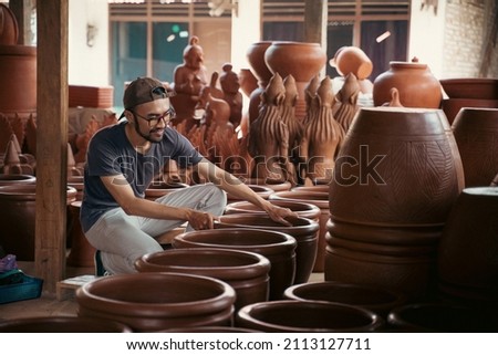 young asian pottery craftsman holding pottery products ready for sale Royalty-Free Stock Photo #2113127711
