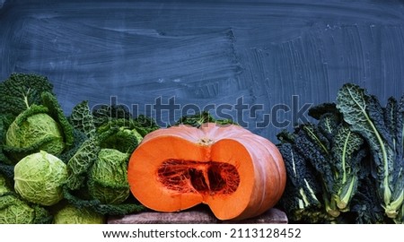 fresh savoy cabbage, a sliced ​​orange squash and green vegetables can be seen at the bottom of the picture in front of a gray slate that has been roughly cleaned and still has streaks of chalk