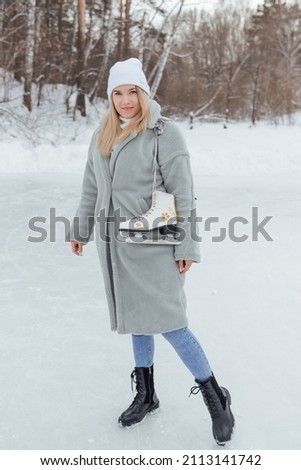 Lovely young woman with ice skates on the ice rink. Girl is going to skating on ice in a winter frosty day