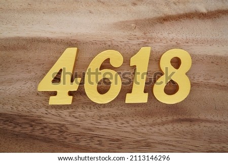 Wooden Arabic numerals 4618 painted in gold on a dark brown and white patterned plank background.
