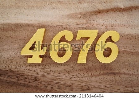 Wooden Arabic numerals 4676 painted in gold on a dark brown and white patterned plank background.